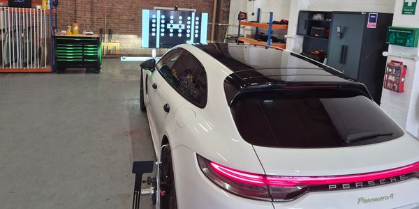White Porsche Panamera in a garage with wheel alignment equipment.