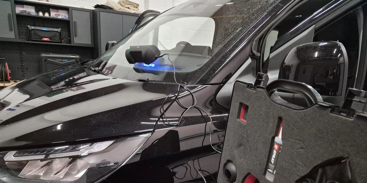 Black car with a device attached to the windshield and a tool case nearby.