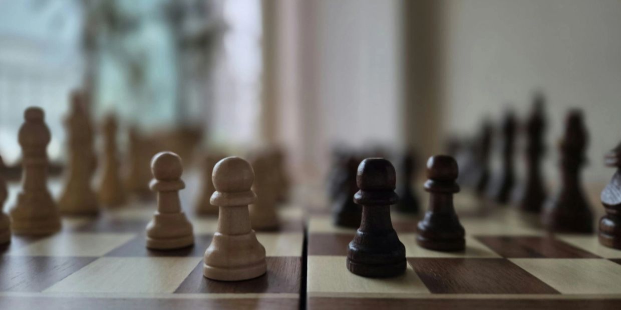 Close-up of chess pawns on a wooden chessboard, white and black pieces facing each other.