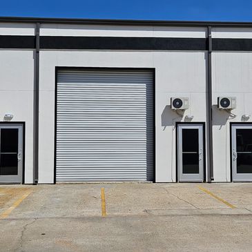 Empty industrial warehouse units with closed roller doors and parking spaces.