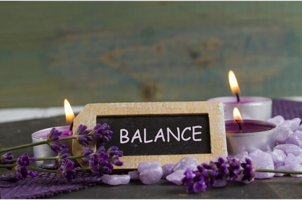 Balance written on chalkboard with candles and purple flowers and stones around the sign.