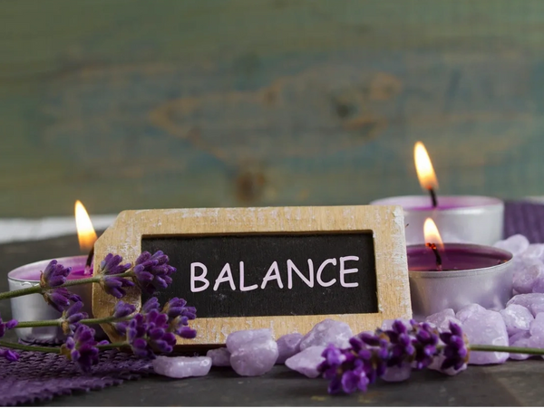 Balance on a sign surrounded by purple candles and lavender flowers.