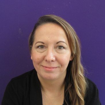 Woman with long blonde hair smiling against a purple background.