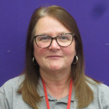 Woman with glasses and long brown hair against a purple background.