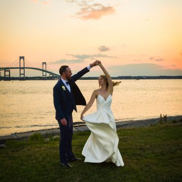 Bride and groom dancing by the water at sunset.