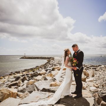 Bride and groom share a moment on rocky shoreline.