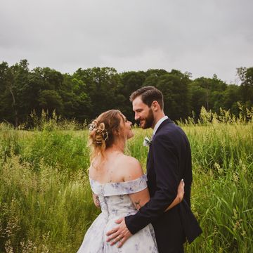 Couple embracing in a lush green field on a cloudy day.
