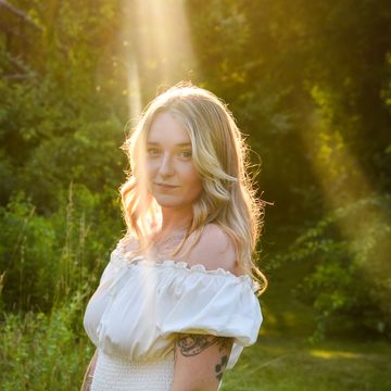 Young woman in white dress standing in sunlight outdoors.