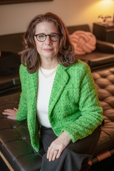 Woman wearing glasses and green jacket sitting on a leather bench.