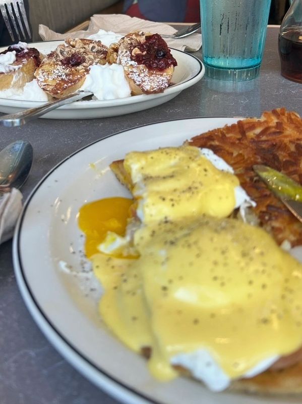 Breakfast with eggs benedict, hash browns, and sweet rolls with cream.