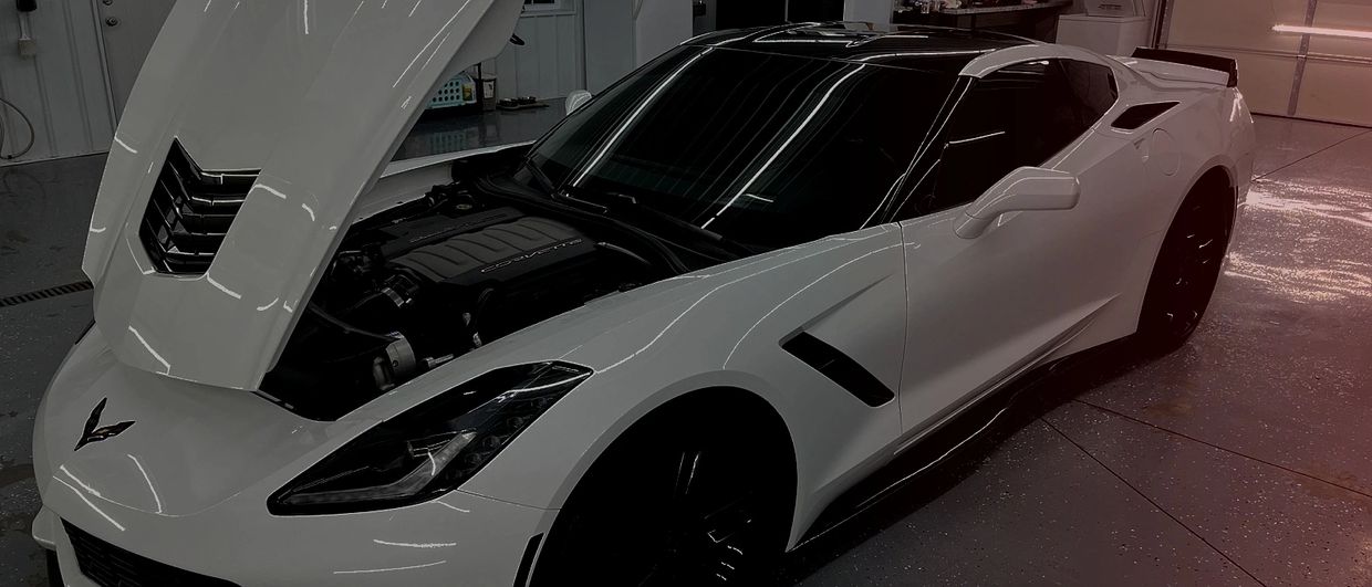 White Chevrolet Corvette with hood open in a garage.