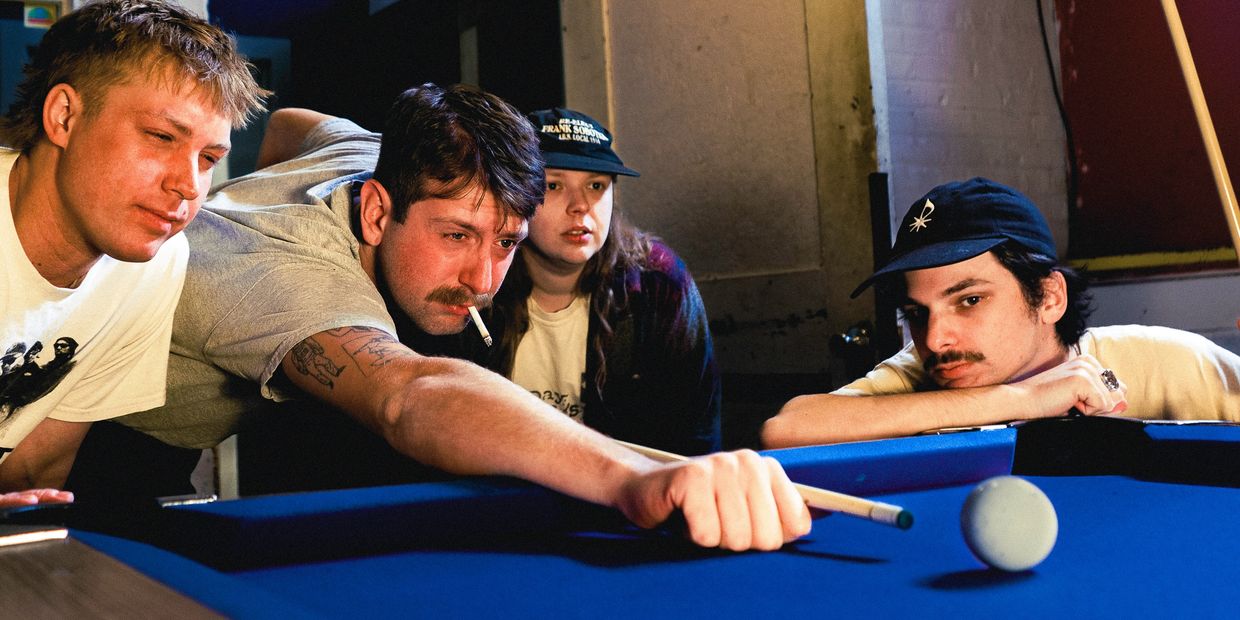 Four friends playing pool, one aiming with a cue stick while others watch.