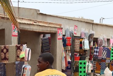 Outdoor market stall selling colorful textiles and bags in a dusty setting.