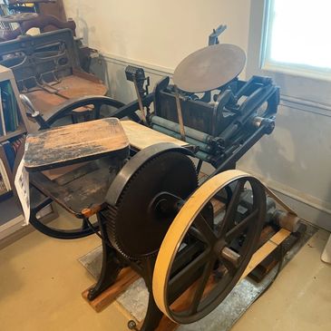 An antique printing press with large wheels and a wooden seat.