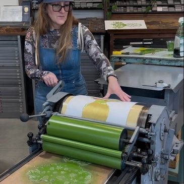A woman operating a printing press with floral designs.