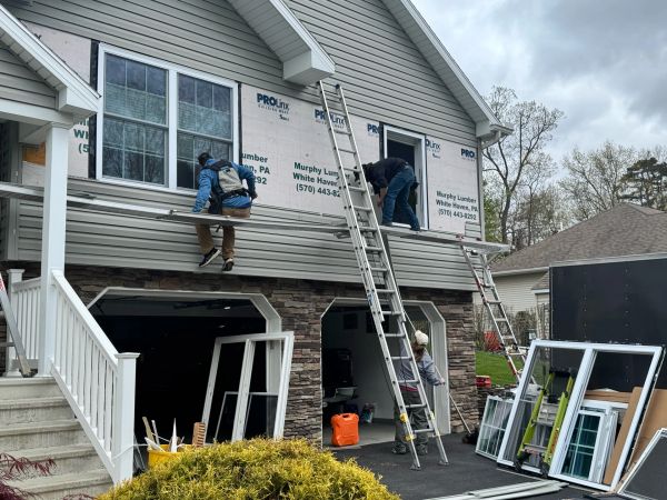Workers installing siding on a house using ladders and scaffolding.