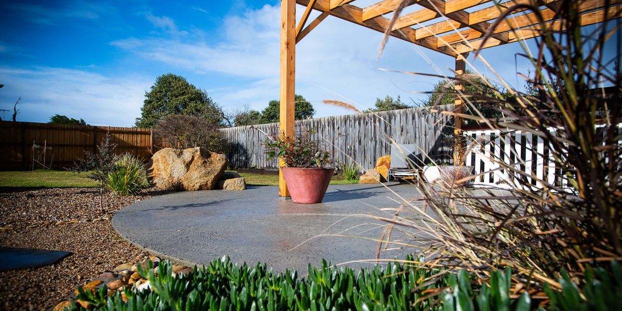Sunny backyard patio with wooden pergola and potted plants.