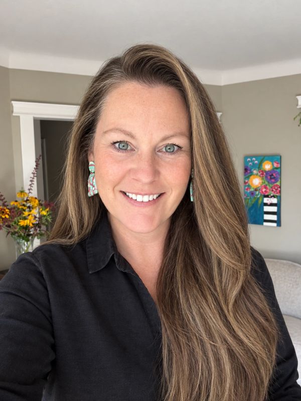 Smiling woman with long hair and patterned earrings.