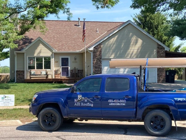 Blue A&amp;T Roofing truck parked outside a beige house.