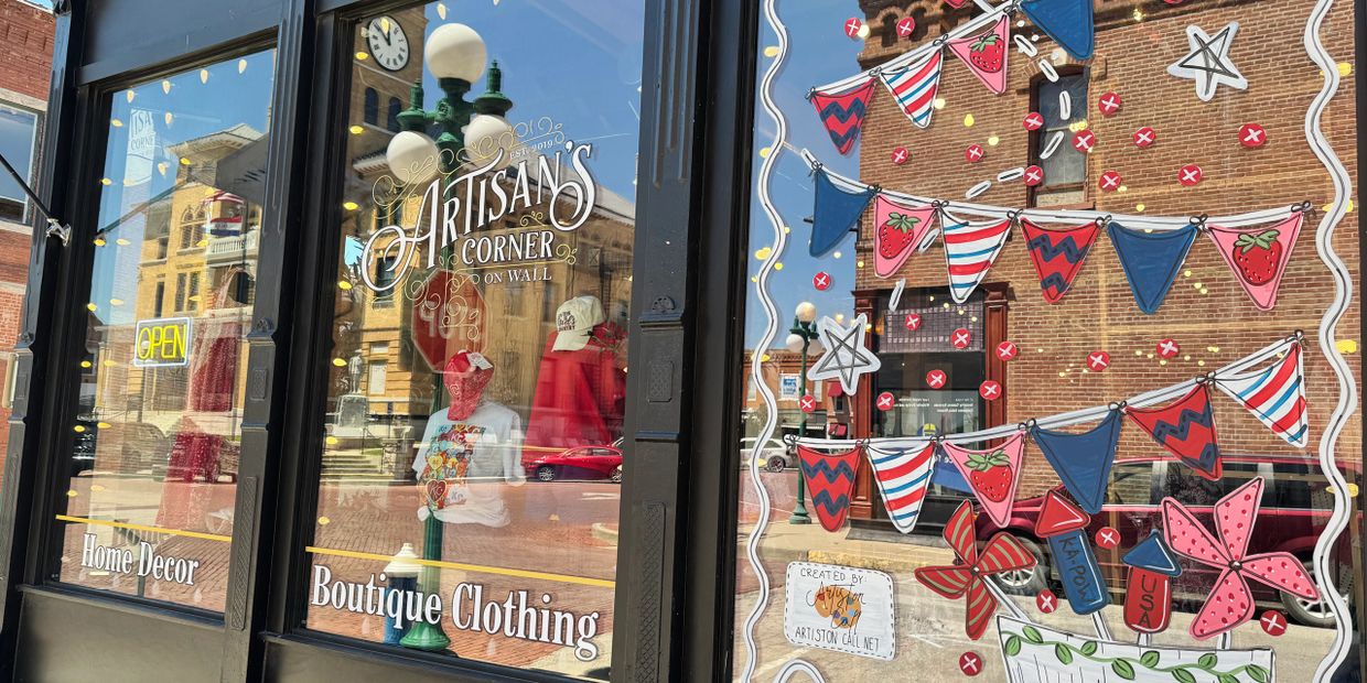 A boutique window with colorful decorations and reflections of a historic street.