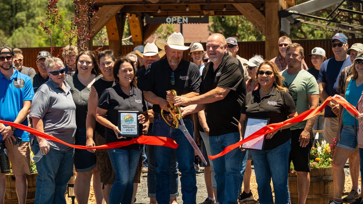 Community ribbon-cutting ceremony with large scissors and plaques under an open wooden structure.
