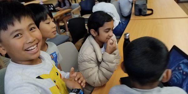 Kids smiling and engaging around a laptop in a classroom.