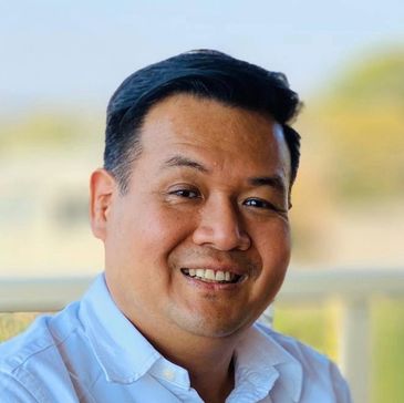 Smiling man in a white shirt with a blurred outdoor background.