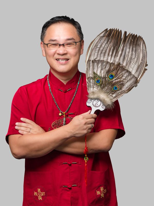 Man in red traditional attire holding a feather fan.