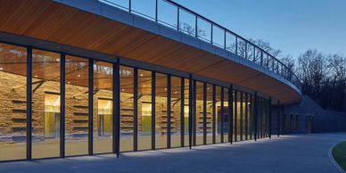 Modern building with glass walls and wooden ceiling during twilight.