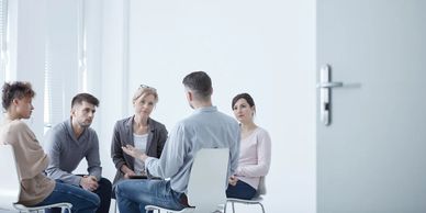 A photo of a group of people sitting in a circle listening to a man speaking.