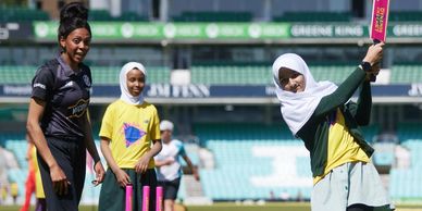 Girls playing cricket on a sunny day in a stadium.