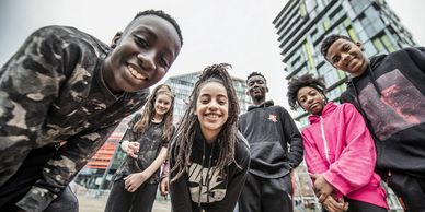 Group of diverse teens smiling outdoors with modern buildings behind them.