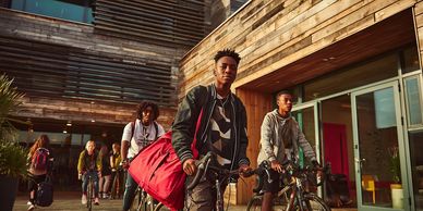 Young people riding bikes near modern wooden buildings.