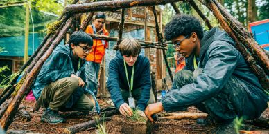 Three boys building a shelter outdoors with a guide nearby.