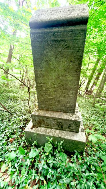 Old weathered gravestone in a forested area with greenery.