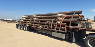 Truck loaded with long metal pipes under blue sky.