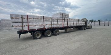 Flatbed truck loaded with materials under cloudy sky.