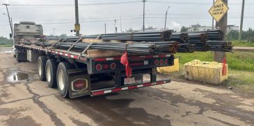 Flatbed trailer loaded with metal pipes on a wet road.
