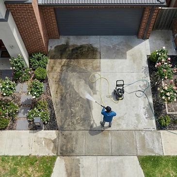 Person pressure washing a driveway, cleaning off dirt and grime.