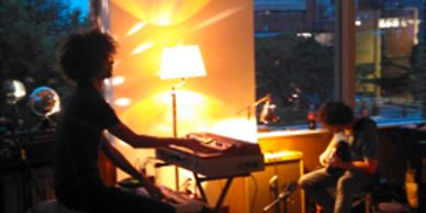 Two musicians playing keyboard and guitar in a warmly lit room.