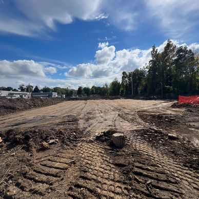 Cleared construction site with tire tracks under a partly cloudy sky.