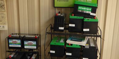 Stacked car batteries on metal shelves in a storage area.