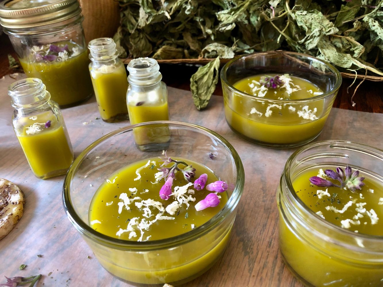 Homemade herbal salves in glass containers with dried herbs in the background.