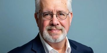 Portrait of an older man with glasses and a beard smiling gently.