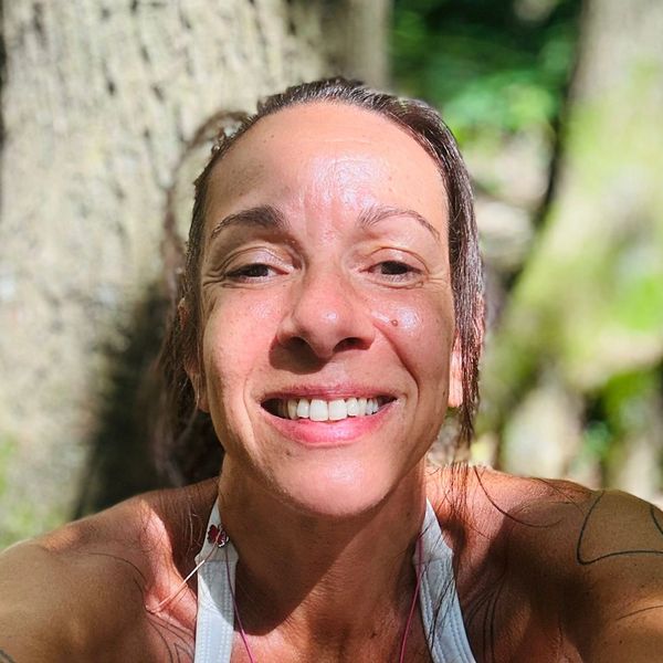 Smiling woman enjoying sunlight outdoors with trees in the background.