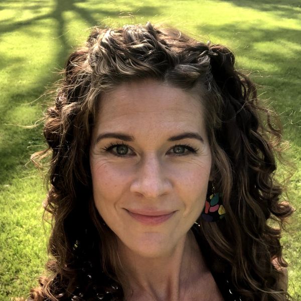 Woman with curly hair smiling outdoors in sunlight.