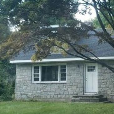 Small stone house with a white door and a large window.