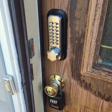 A wooden door with a keypad lock and a combination padlock on the handle.