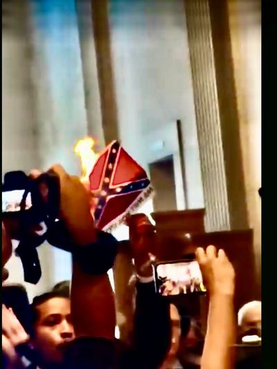 Person holding a burning Confederate flag inside a building.