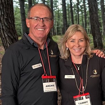 Two smiling people wearing name tags in a forest setting.